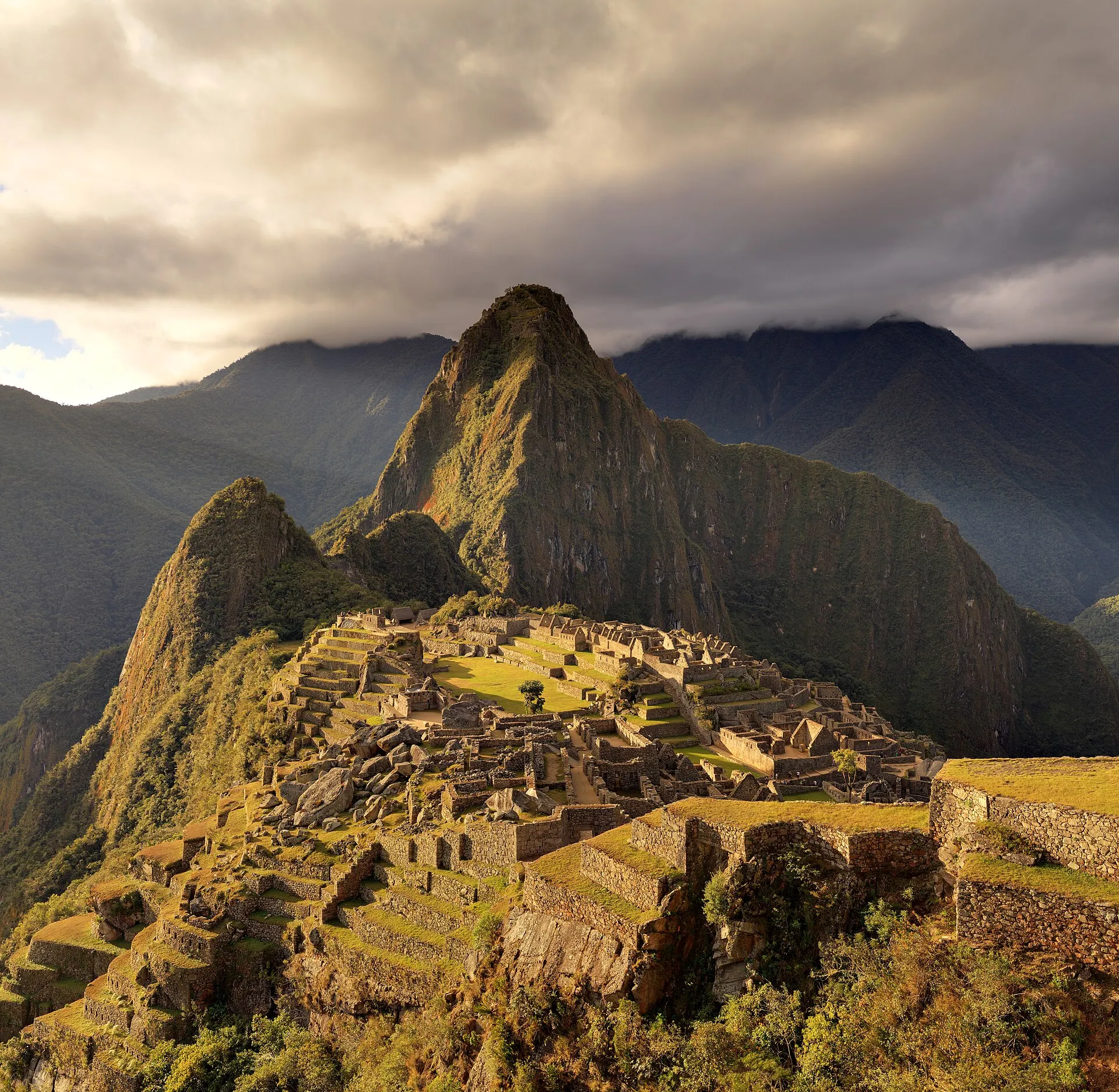 The ancient stone city of Machu Picchu high in the mountains of Peru, with stone terraces and the pointy peak of Huayna Picchu behind it.